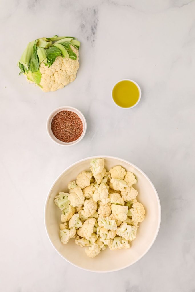 Cauliflower, olive oil, and seasonings measured out on a white marble table