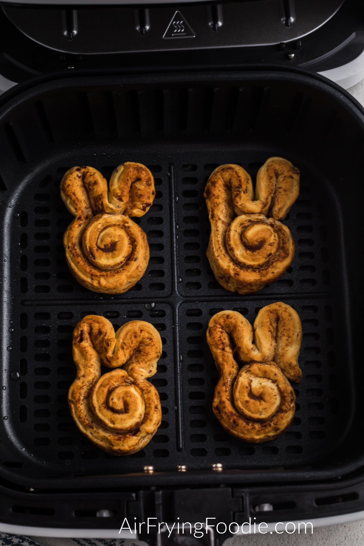 Air fried cinnamon rolls in the shape of bunnies in the air fryer basket.