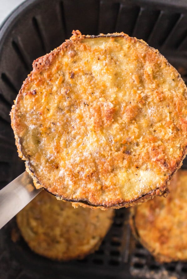 Cooked and crispy Air fryer eggplant being lifted out of the basket of the air fryer.