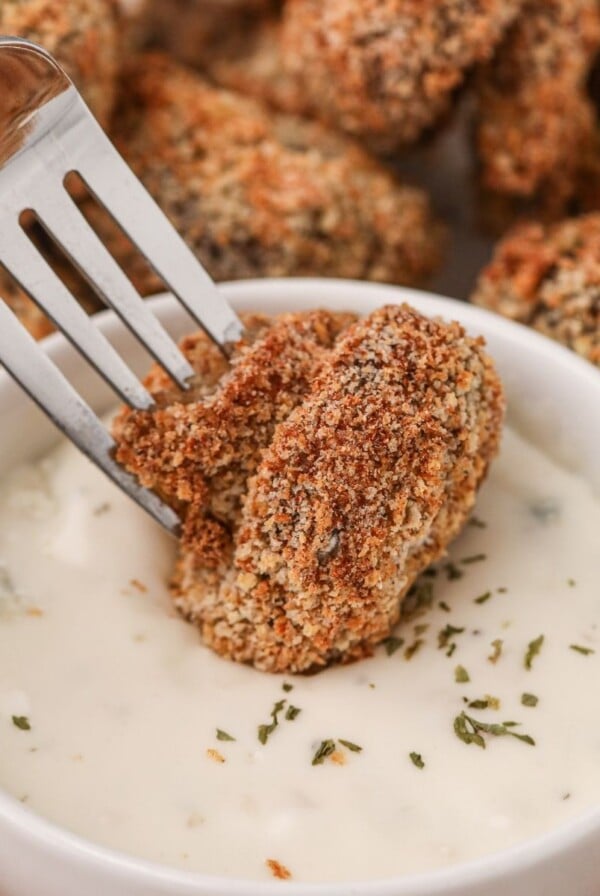 Golden brown fried mushroom being dipped into ranch dressing