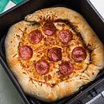 Air fryer pizza that has been fully cooked and is in the basket of the air fryer.