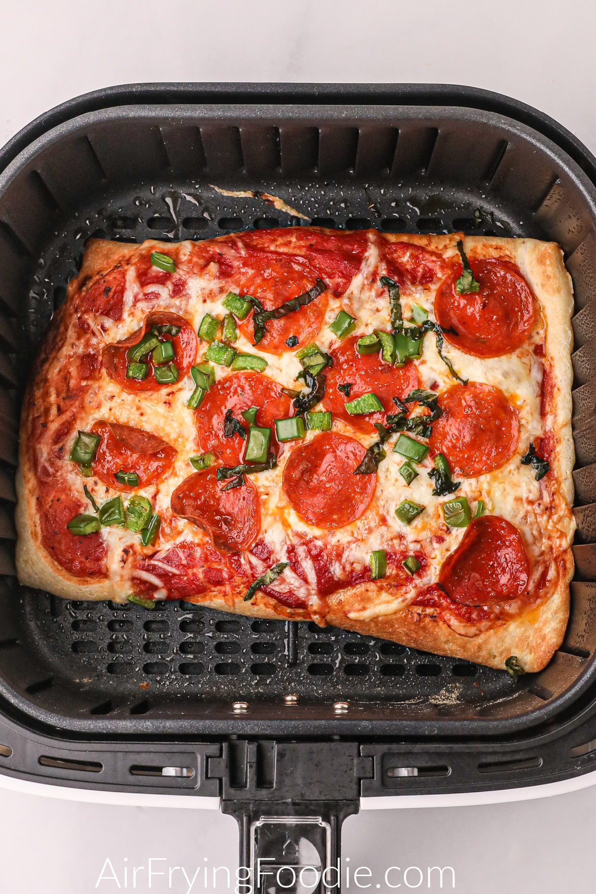 Fully cooked pizza in the basket of the air fryer, ready to serve.