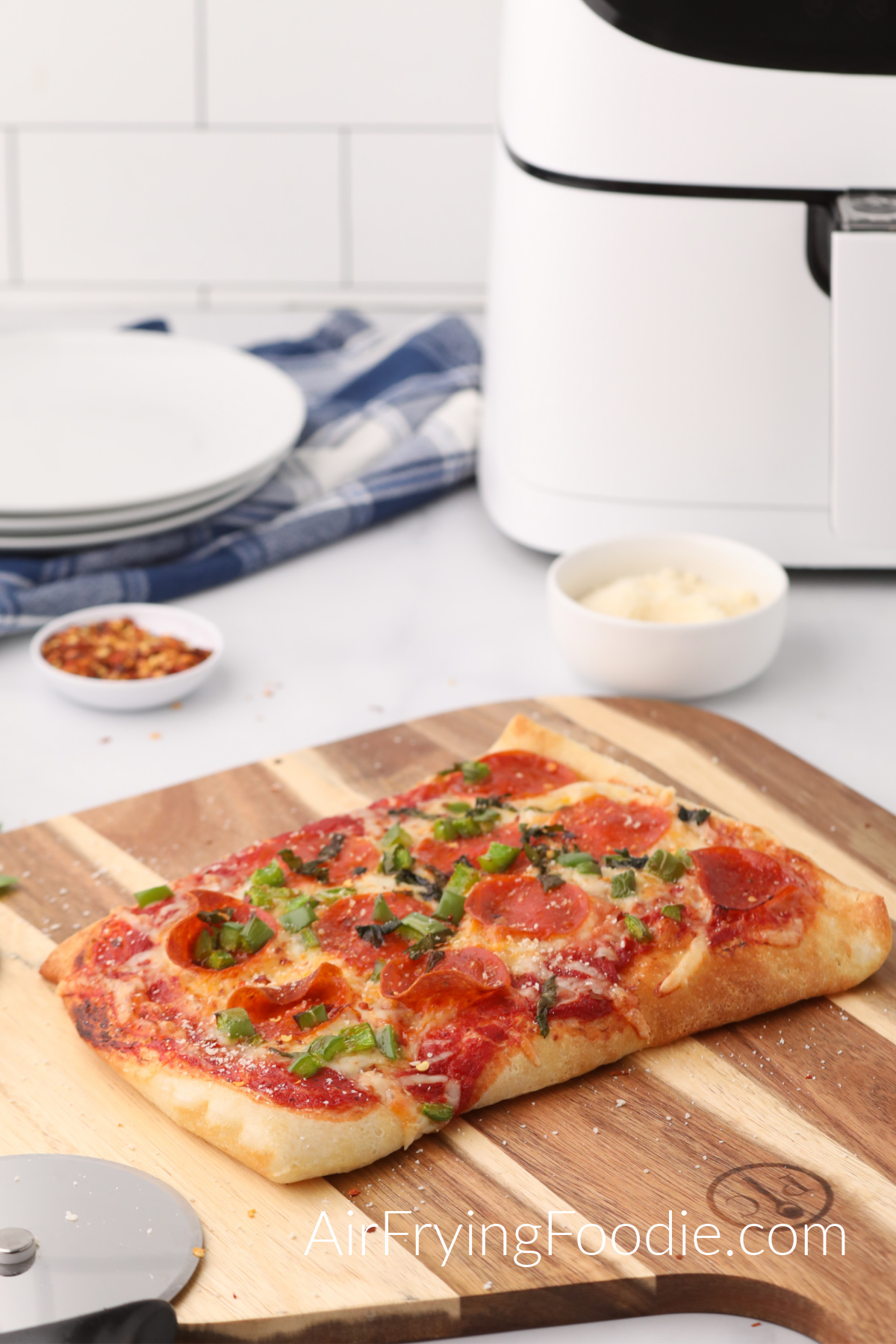 Air Fryer Pizza made in the Cosori air fryer on a cutting board with ingredients and the air fryer in the background. 