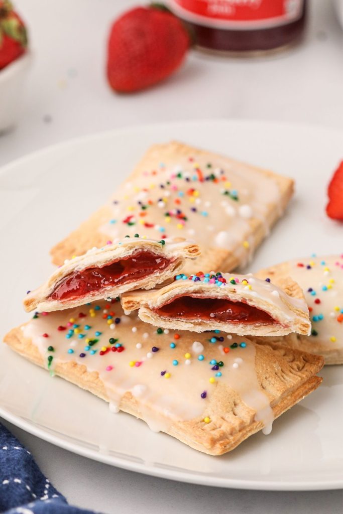 Golden flaky pop tarts filled with strawberry am and glazed on a white plate