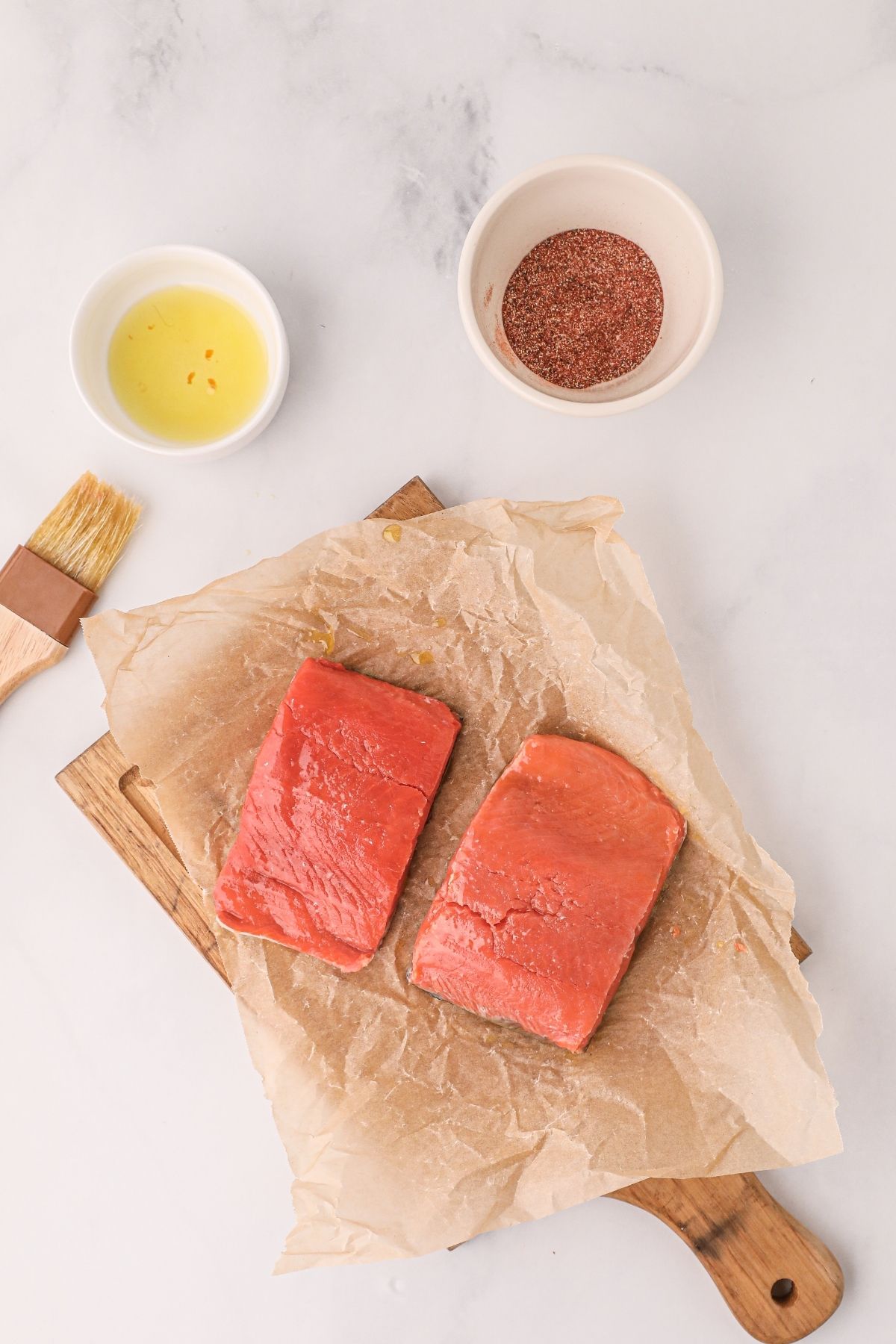 Salmon on a board with seasonings mixed on the table with a brush and oil