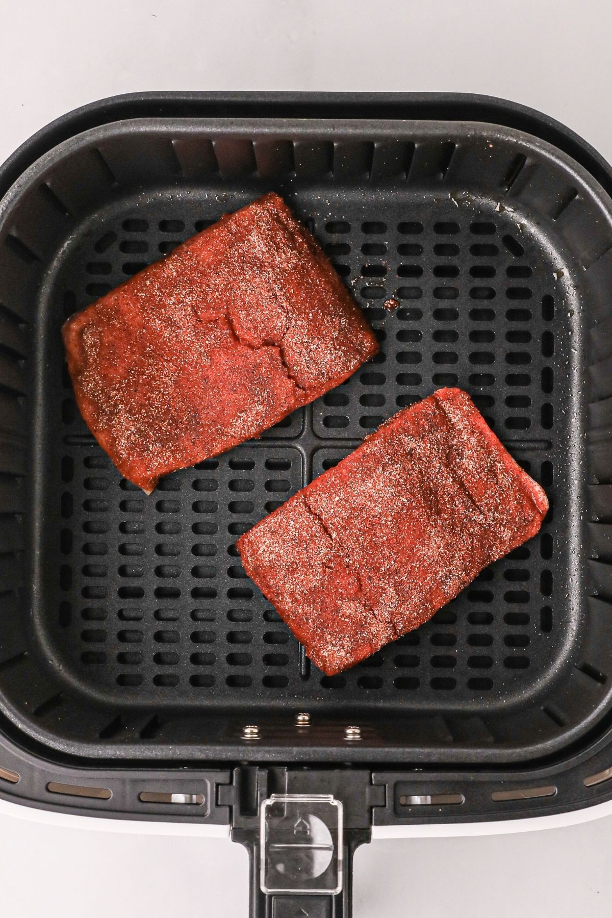 Seasoned filets in an air fryer basket before being cooked