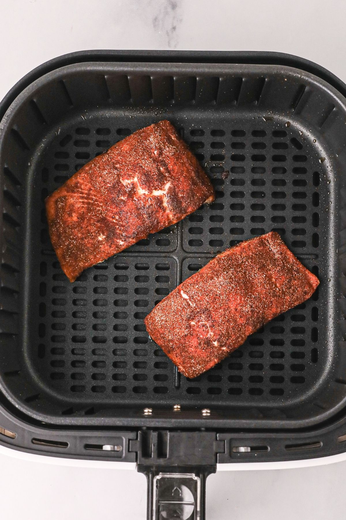 Seasoned salmon filets in the air fryer basket after being cooked