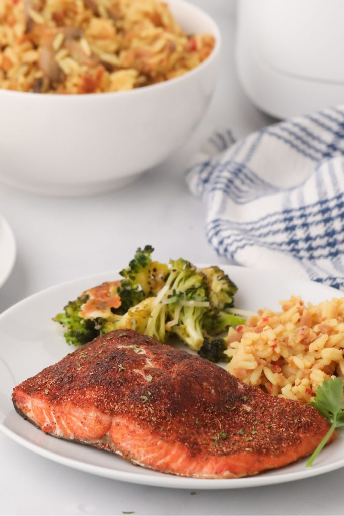 Seasoned cooked salmon on a white plate with rice and broccoli