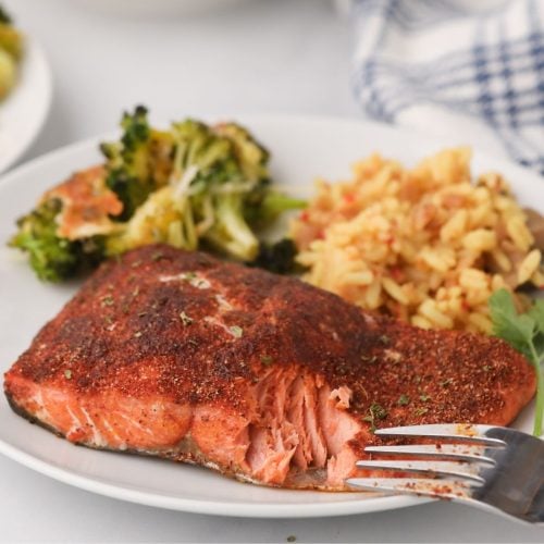 Flaky seasoned salmon on a white plate with rice and broccoli with a fork bite