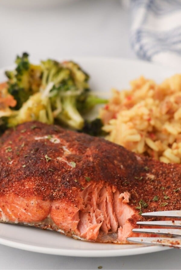 Flaky seasoned salmon on a white plate with rice and broccoli with a fork bite