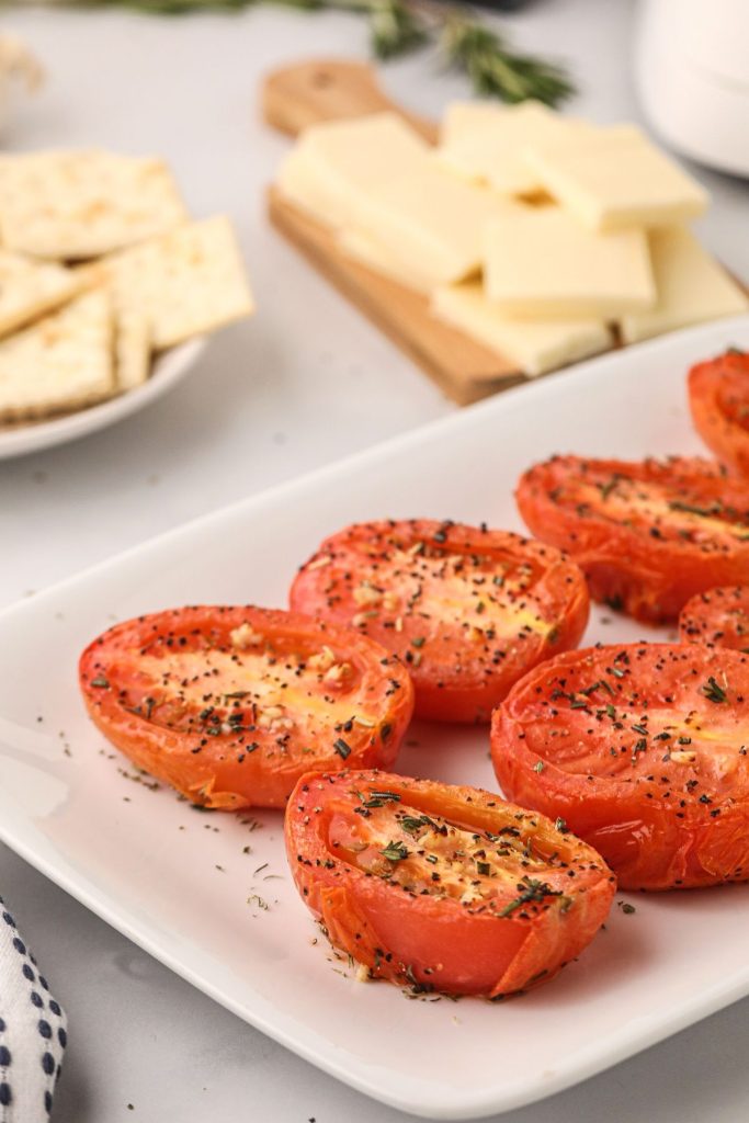Seasoned juicy red tomatoes after being air fried and served on a white plate with cheese and crackers