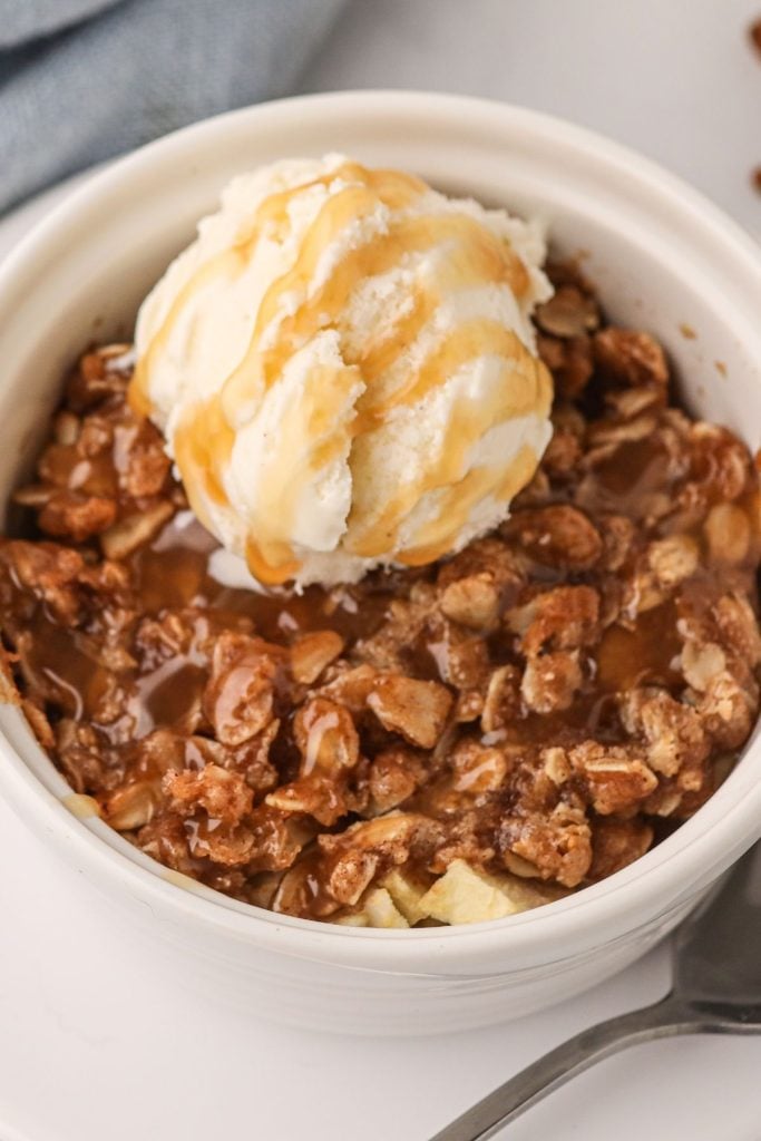 Close up photo of apple crisp topped with oats and ice cream, drizzled in caramel sauce.