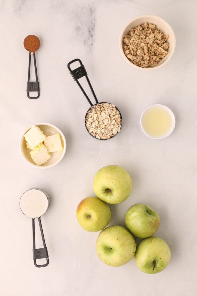 Ingredients needed to make apple crisp, measured out and on a white marble table