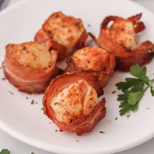 Bacon wrapped scallops on a white plate made in the air fryer.