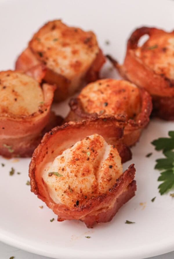 Bacon wrapped scallops on a white plate made in the air fryer.