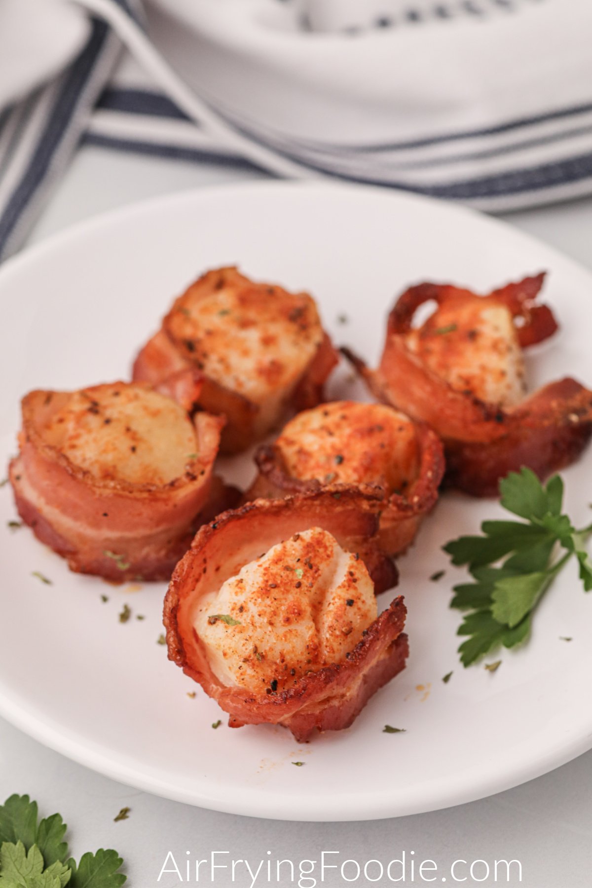 Air fryer bacon wrapped scallops fully cooked and on a white plate, ready to serve.