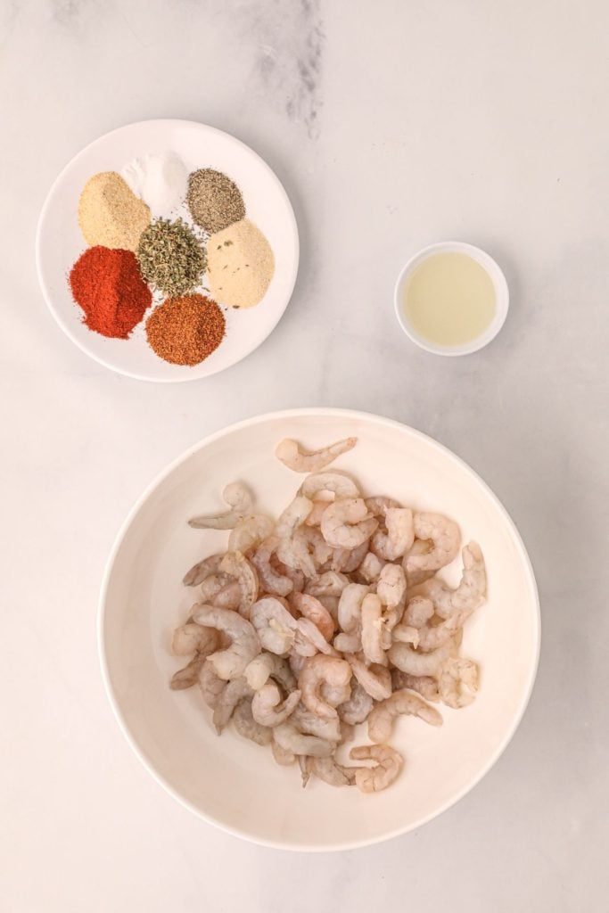 Shrimp and seasonings measured in a bowl on a white marble table.