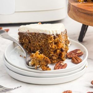 Slice of carrot cake on a white plate with a fork holding a bite of the cake