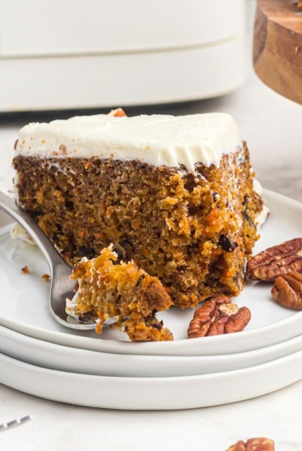 Slice of carrot cake on a white plate with a fork holding a bite of the cake