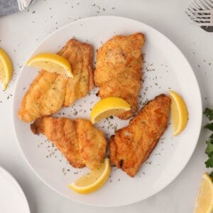 Air fried catfish on a white plate with lemon wedges.