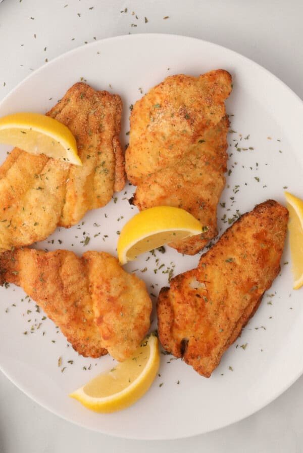 Air fried catfish on a white plate with lemon wedges.