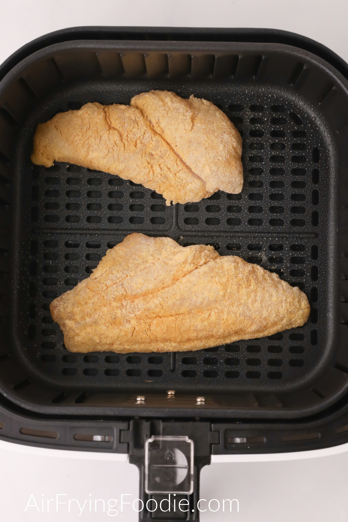 Breaded catfish fillets in the basket of the air fryer, ready to cook.