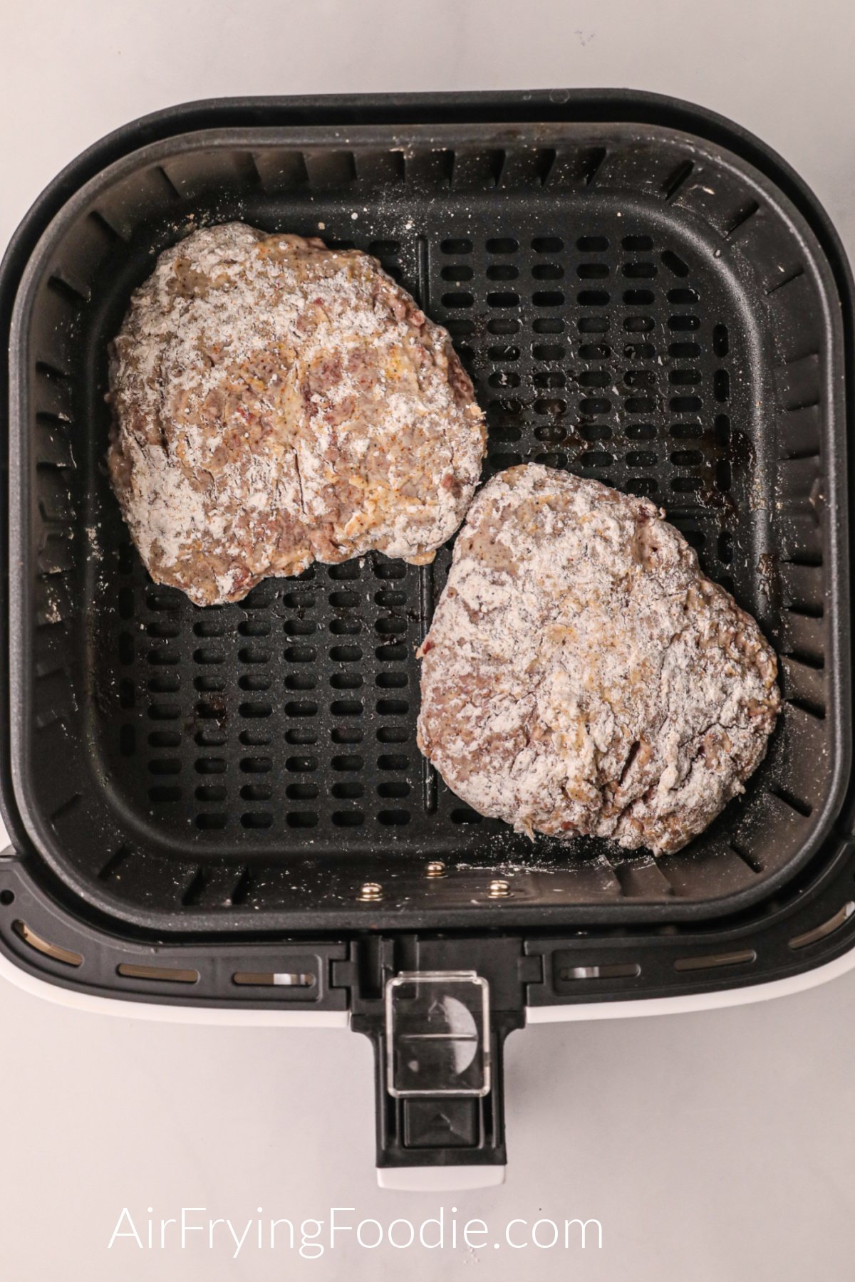 Breaded round steaks in the basket of the air fryer, ready to cook.