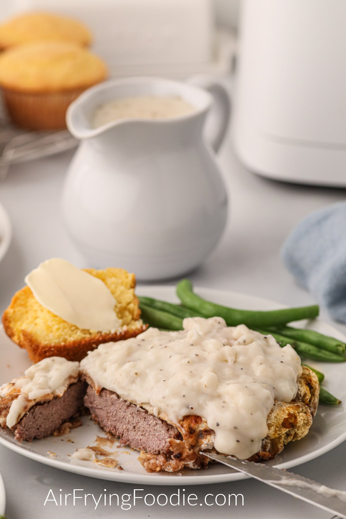 Chicken fried steak made in the air fryer and served on a plate with green beans and cornbread. 