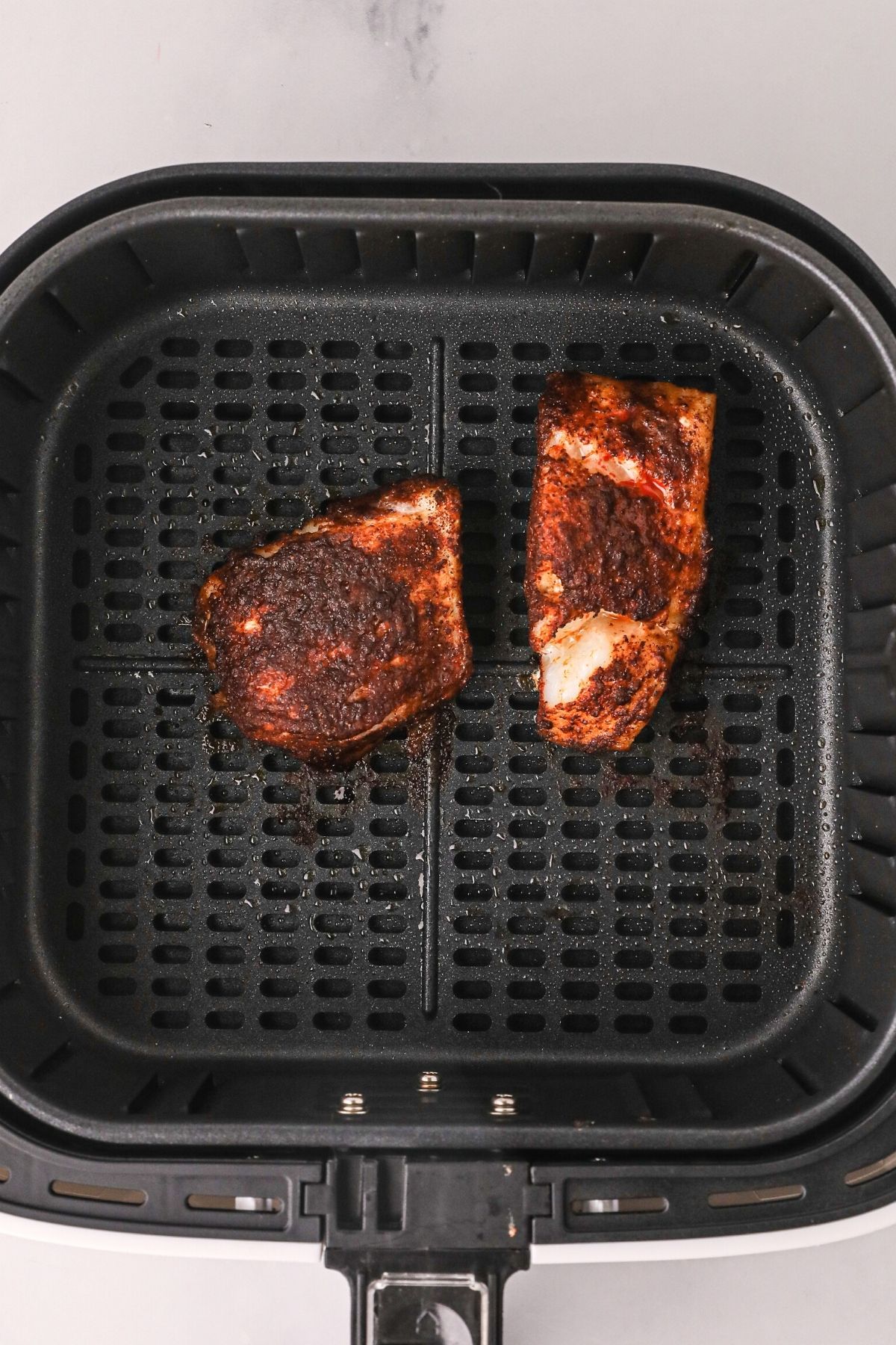 cod filets in the air fryer basket after being cooked in the air fryer