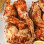 Golden orange seasoned crispy cooked frog legs on a white plate with a garnish of lemon wedges