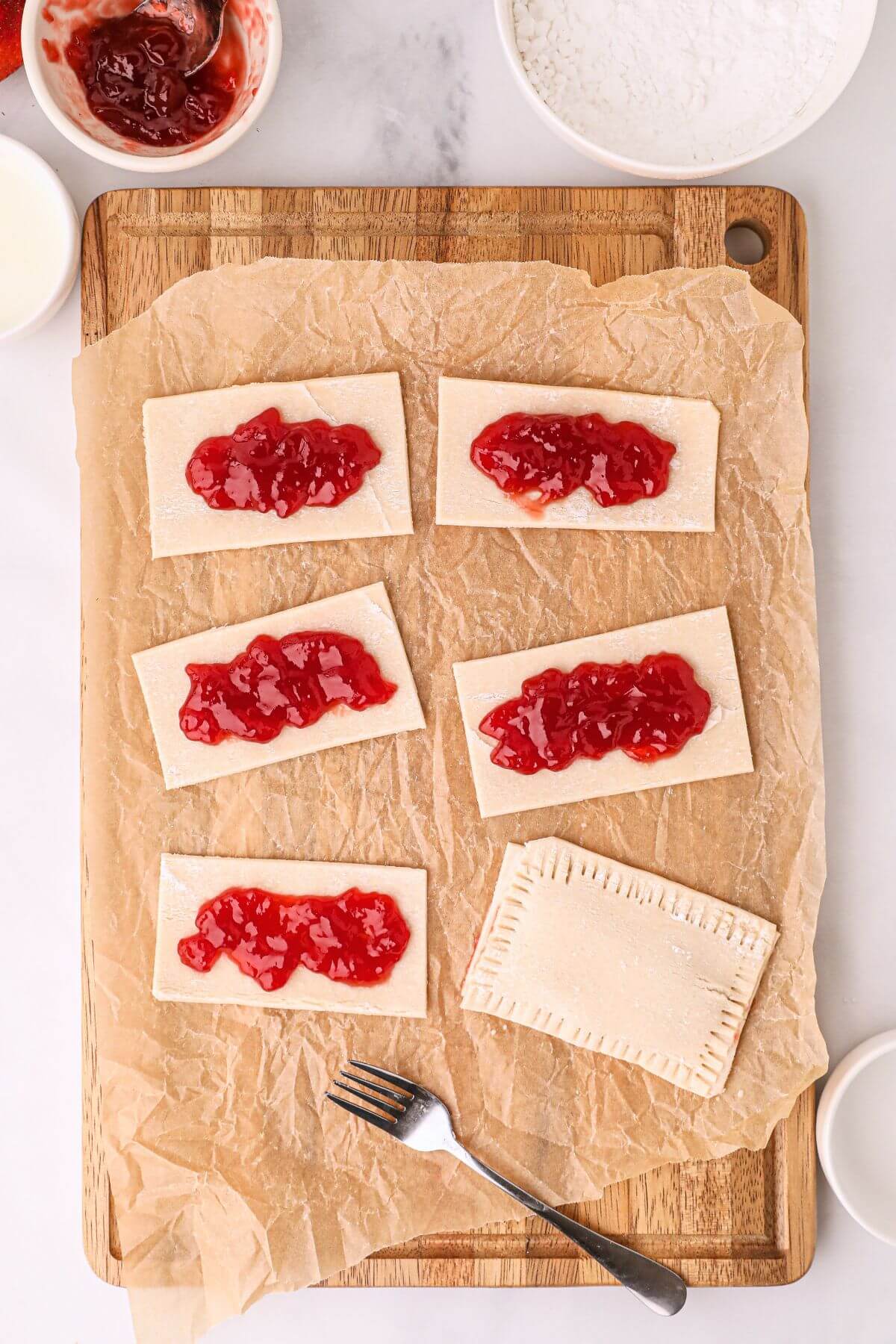 Rectangles of pastries on a wooden cutting board topped with jam.
