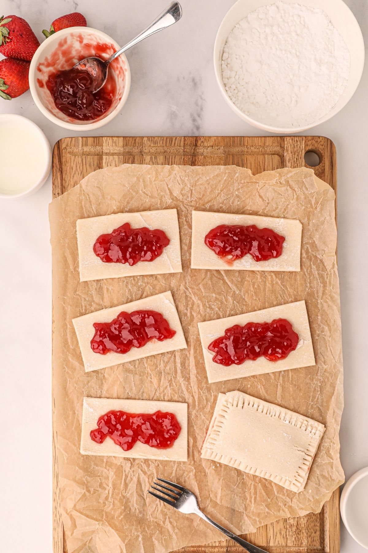 Pastry rectangles topped with strawberry jam on a cutting board