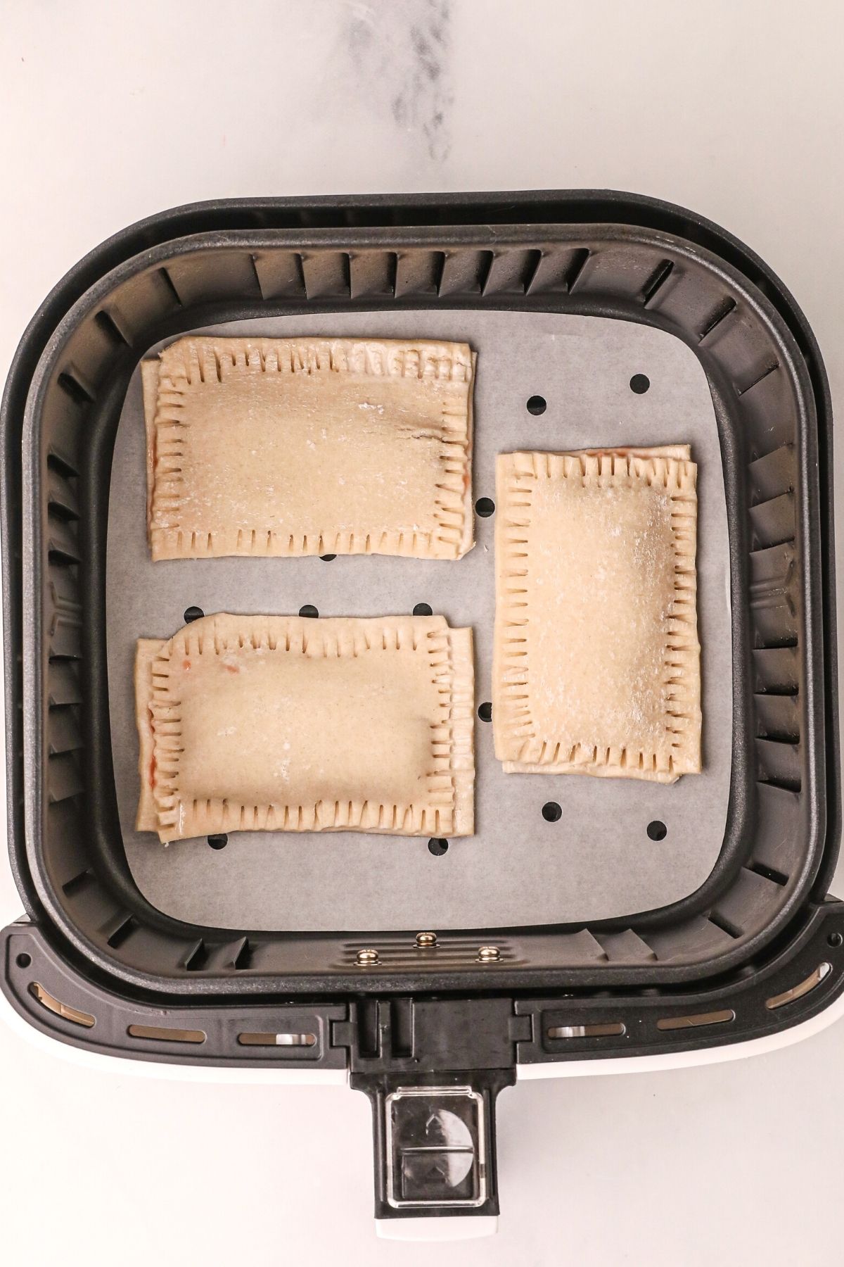 uncooked pop tarts in the air fryer basket, lined with parchment paper