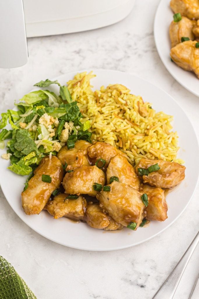 Golden crispy chicken on a white plate served with rice and lettuce, tossed in a sweet and sour sauce.
