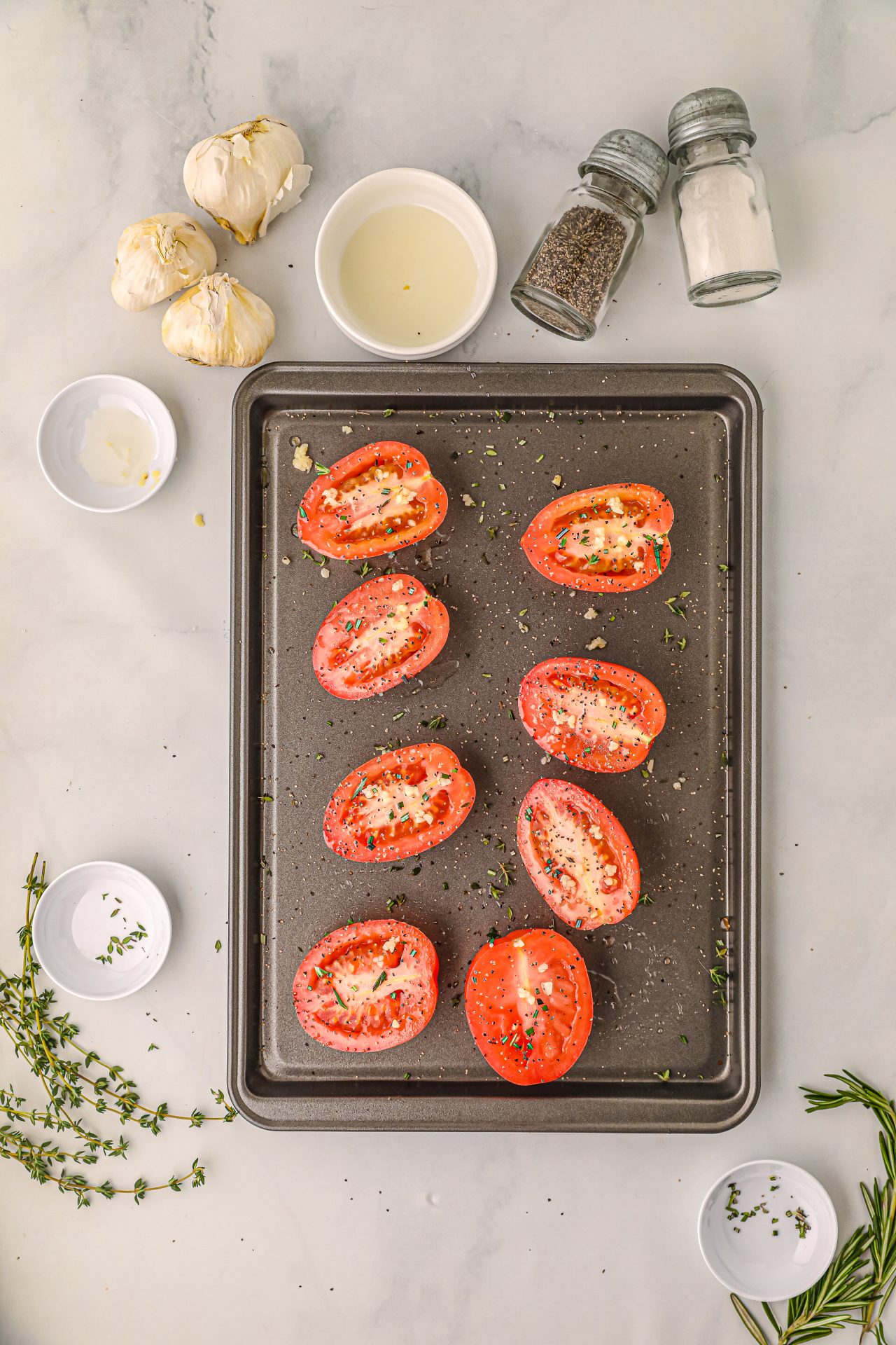 Sliced tomatoes on a baking sheet being drizzled with olive oil and seasonings