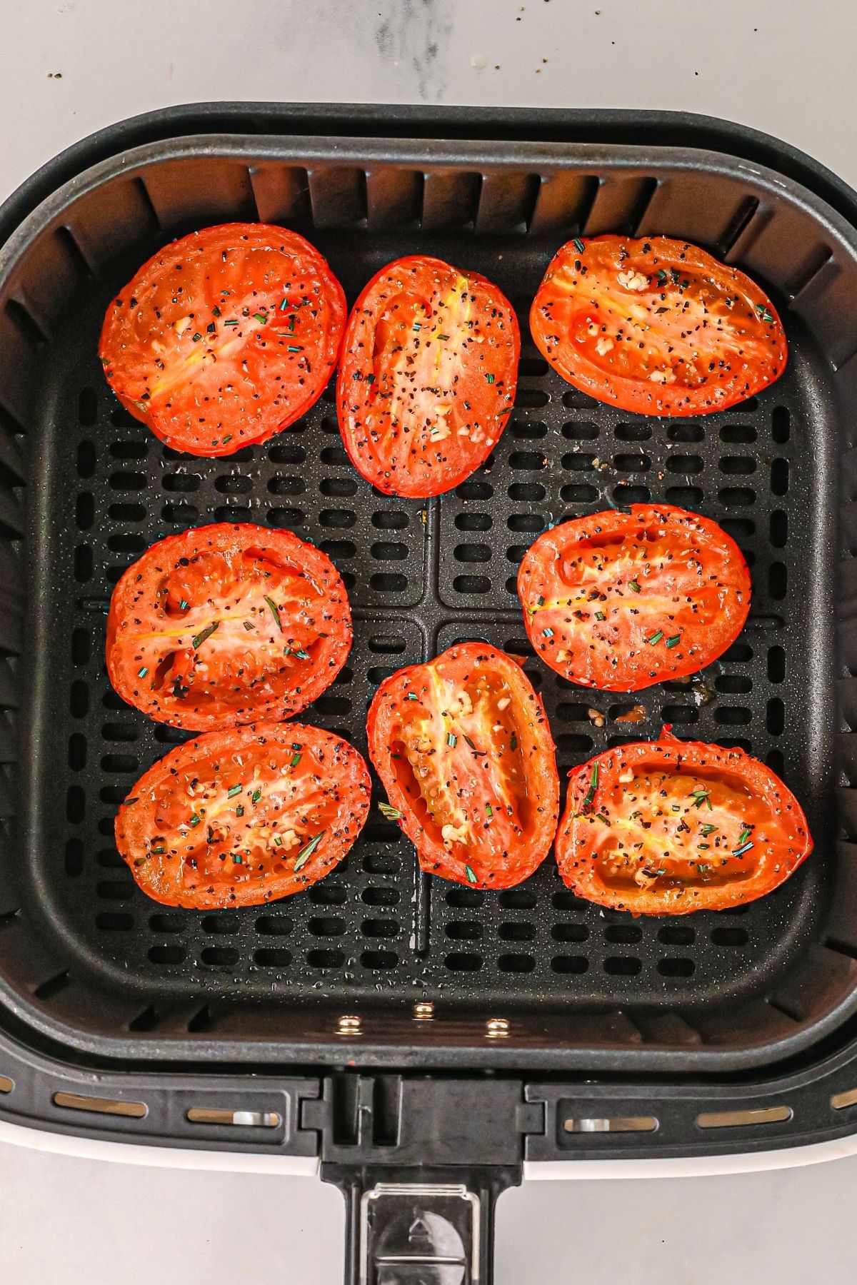 Cooked tomatoes in the air fryer basket after being seasoned. 