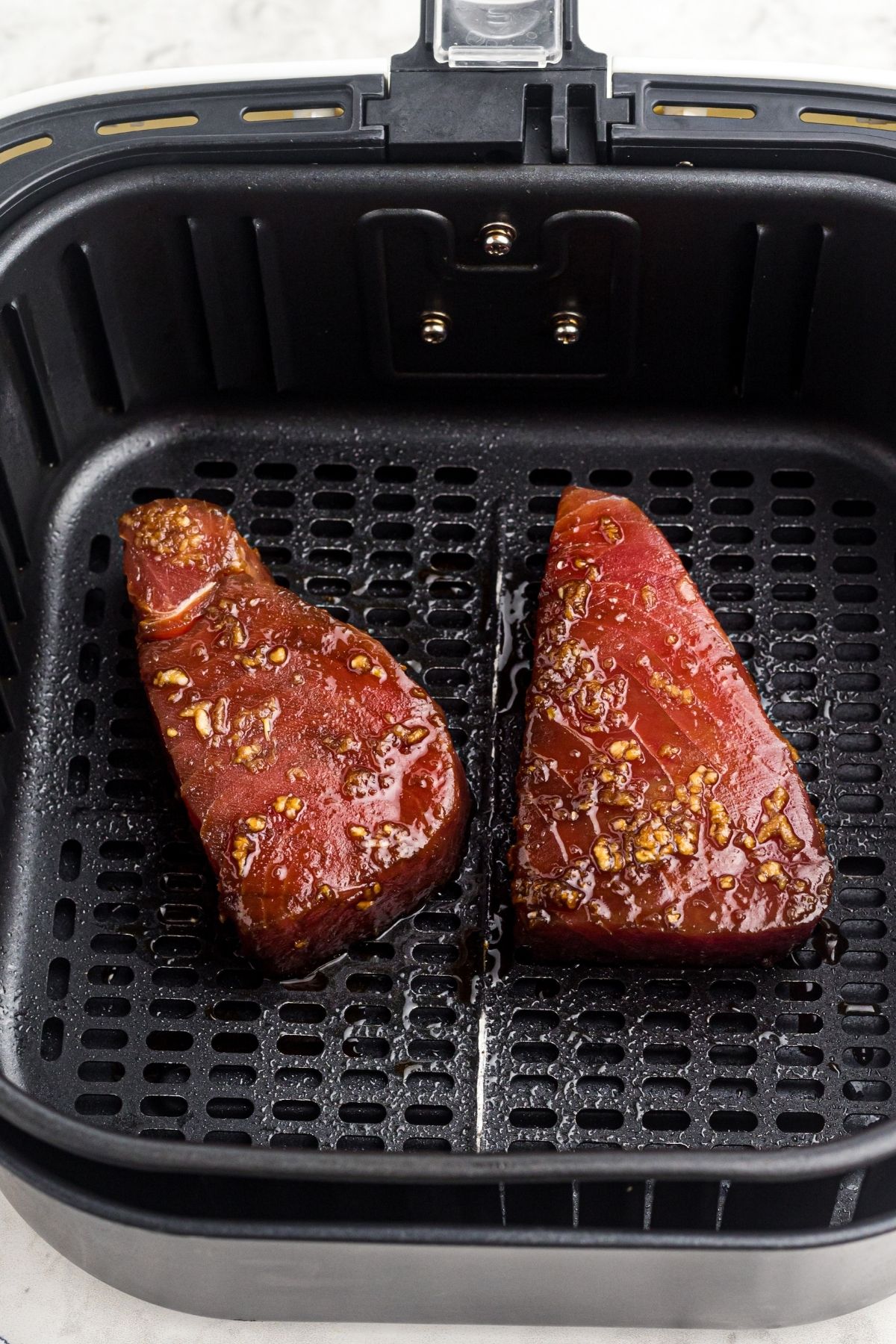 Marinated tuna steaks in the air fryer basket before being cooked