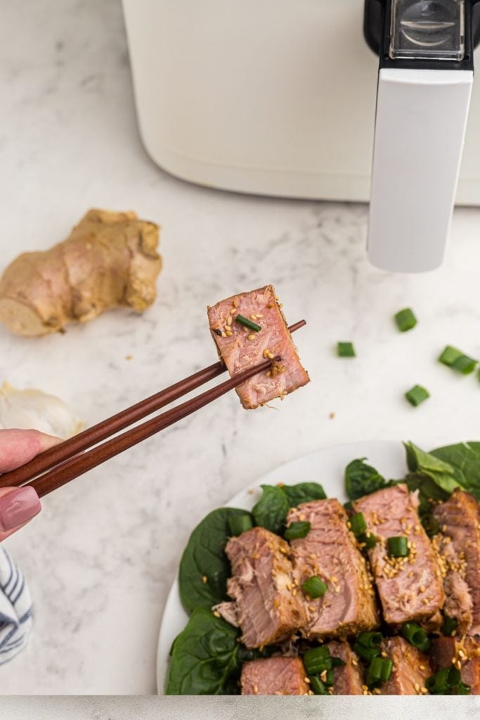 Chopsticks holding a piece of tuna steak garnished with sesame seeds