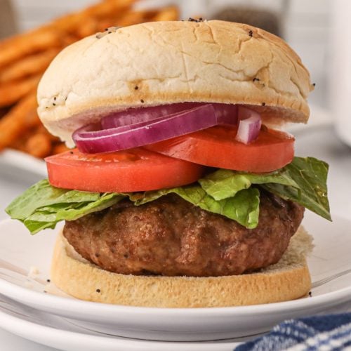 Air fryer turkey burger patty on a bun with lettuce, tomato, and onion.