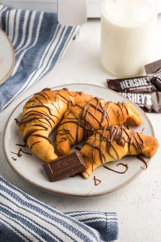 Golden chocolate filled croissants on a white plate served with milk and chocolate drizzles