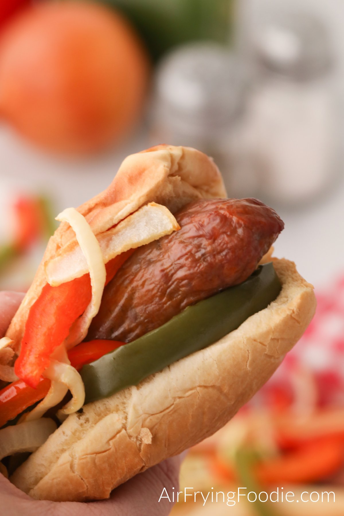 Italian Sausage made in air fryer with peppers and onion and served with a bun - hand holding the bun and ready to eat.