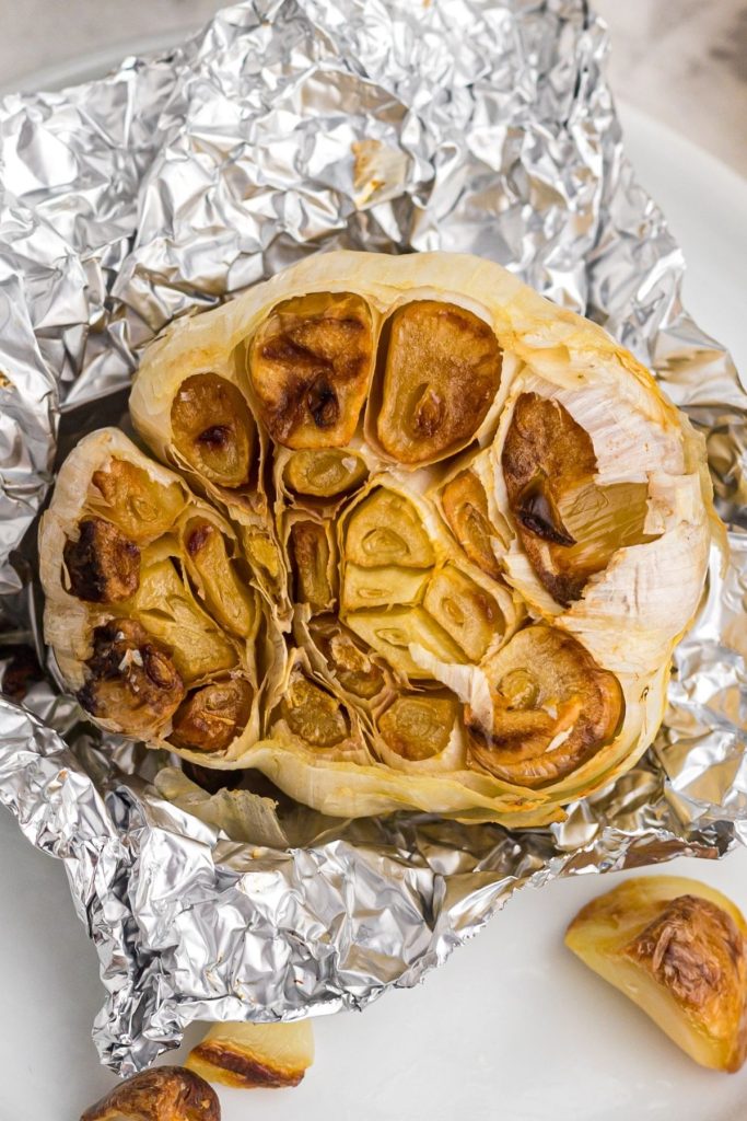 Up close photo of golden brown roasted garlic bulb on a small piece of foil