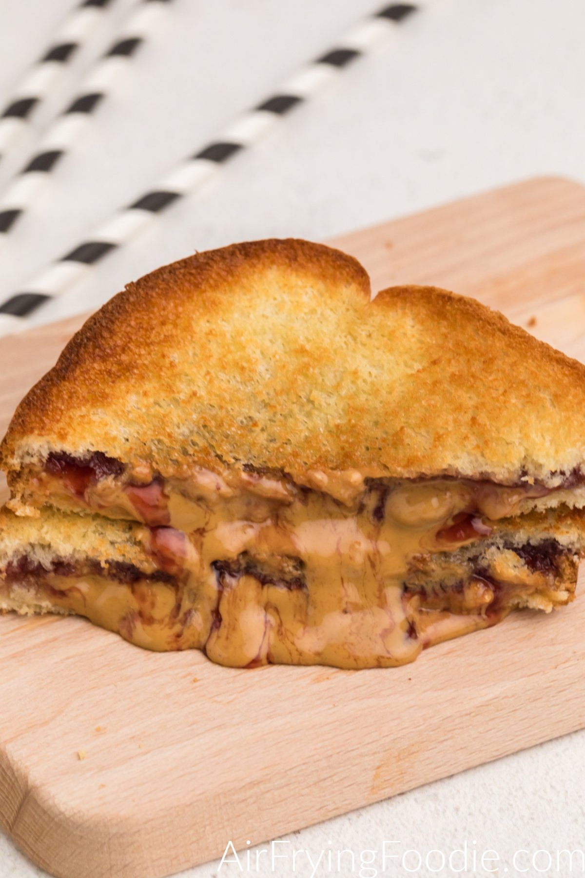 Fried peanut butter and jelly sandwich sliced in hald with melted peanut butter oozing out onto the cutting board.