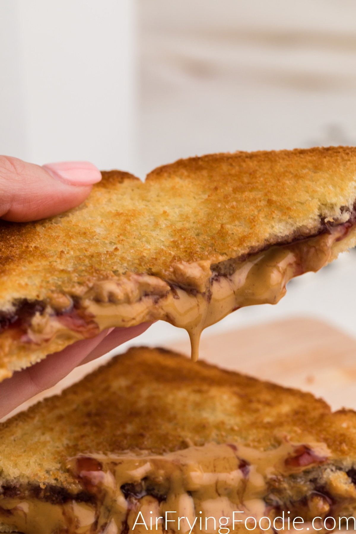 Hand holing a dripping melted peanut butter and jelly from a cut sandwich.