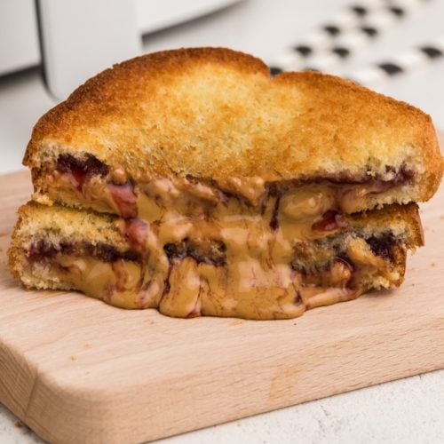 sliced fried peanut butter and jelly sandwich made in the air fryer, golden brown and with melted peanut butter and jelly oozing onto the cutting board.