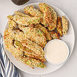 Overhead photo of air fried avocado fries on a white plate with dipping sauce.