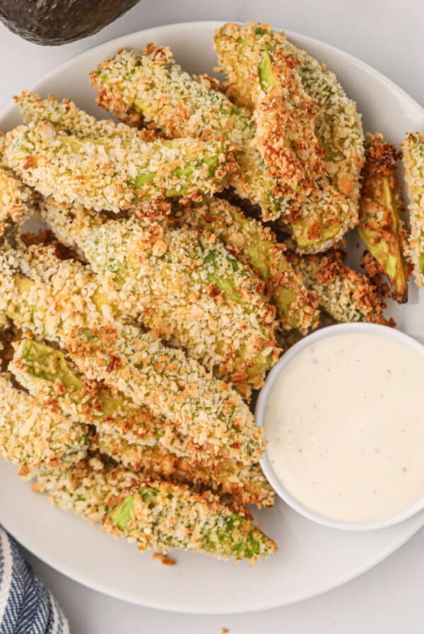 Overhead photo of air fried avocado fries on a white plate with dipping sauce.