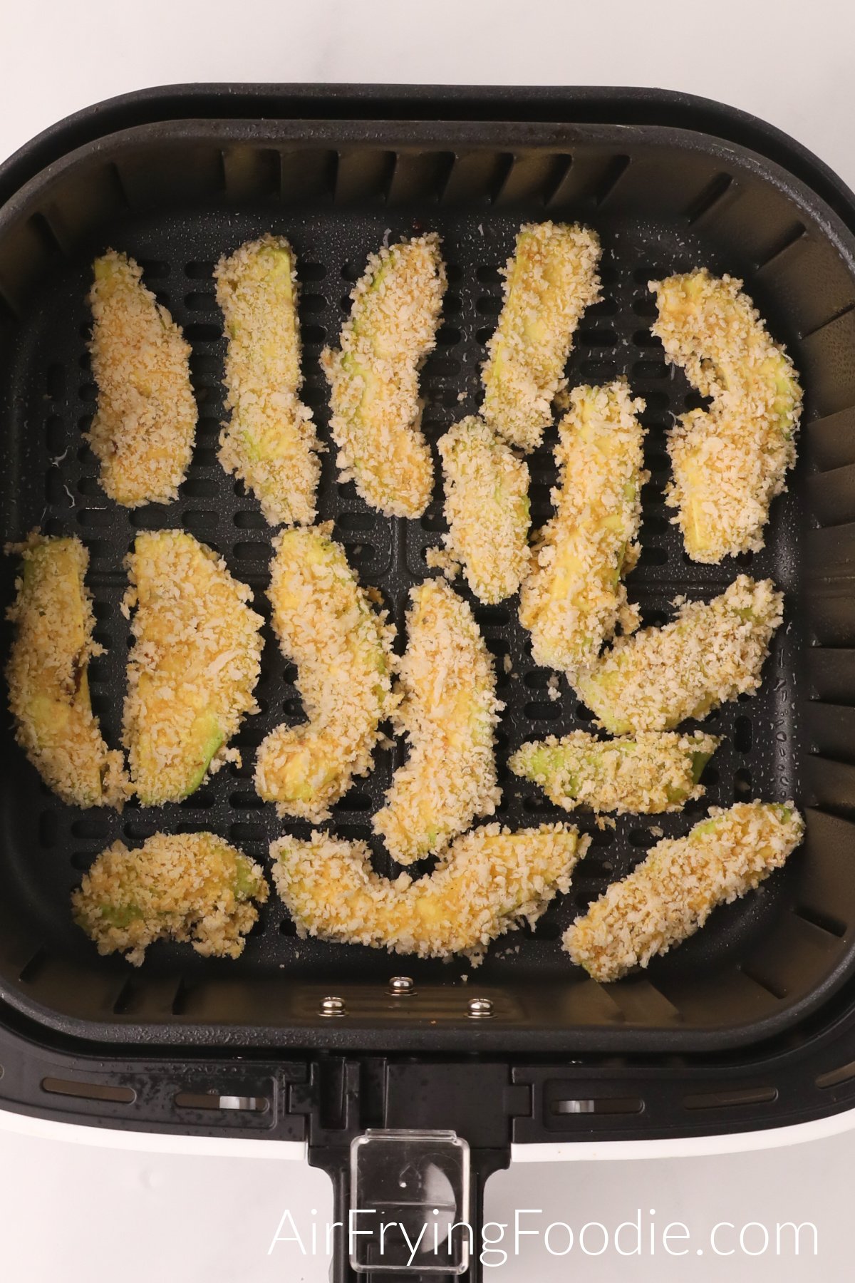 Avocado fries in the basket of the air fryer ready to be cooked.