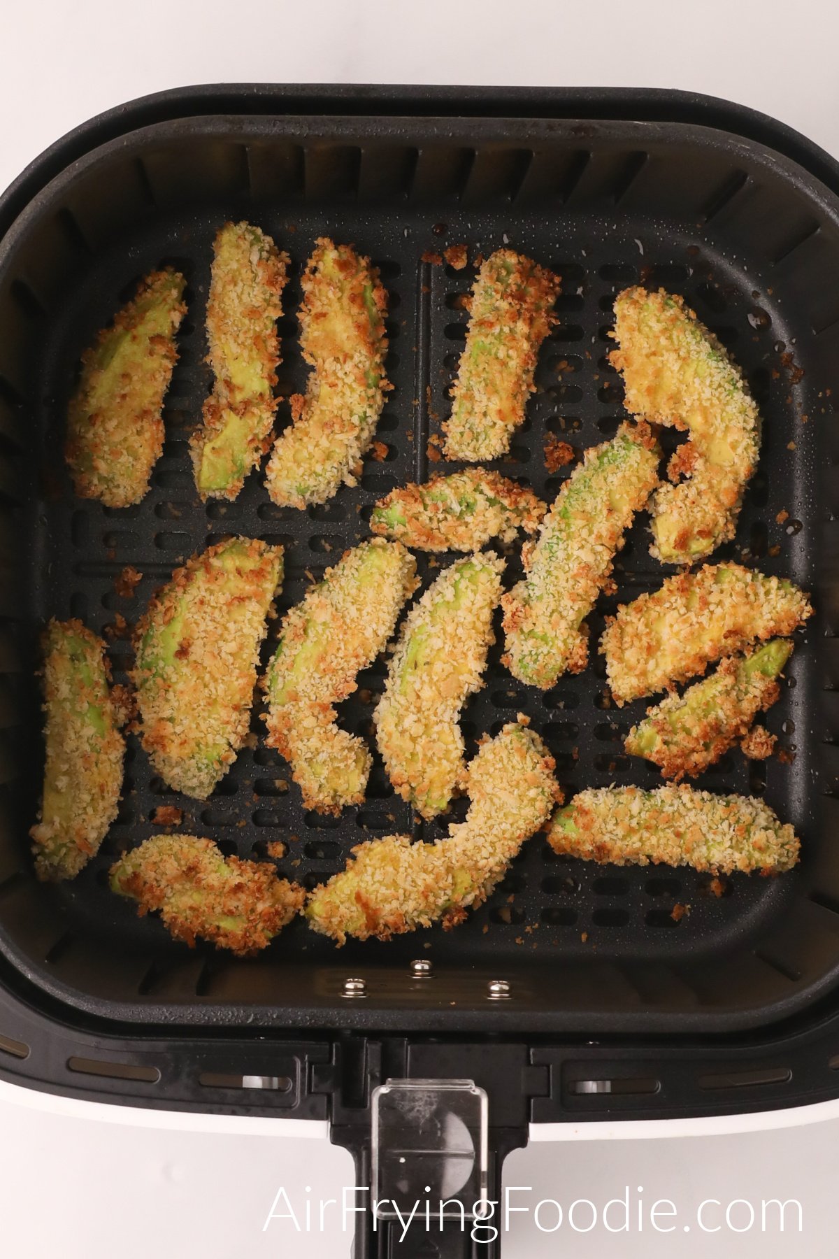 Avocado fries in the basket of the air fryer, fully cooked and ready to serve.