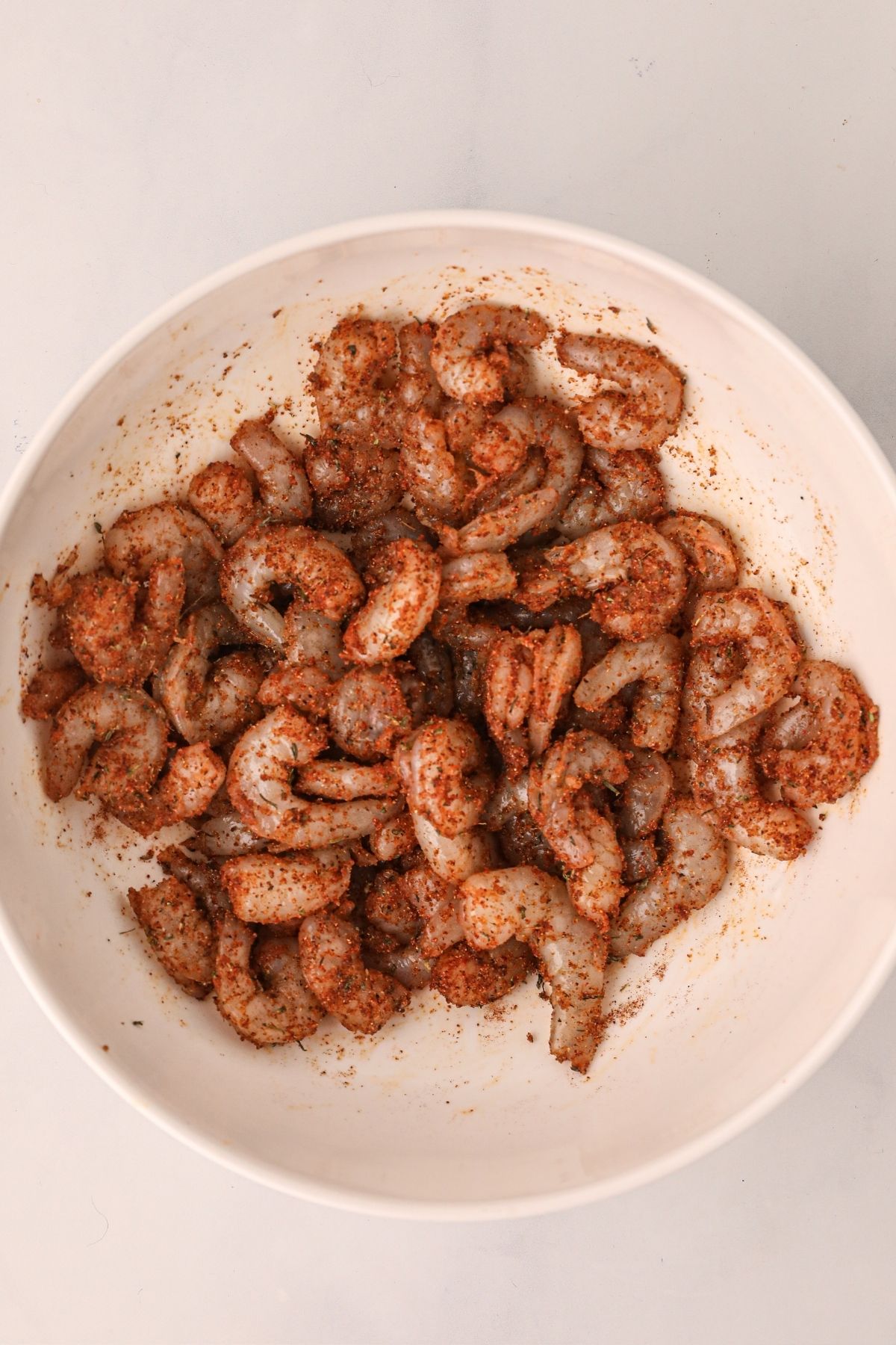 Uncooked shrimp in a white bowl tossed with seasonings before being cooked in the air fryer